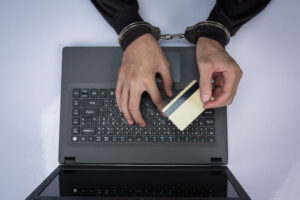 golpe da portabilidade do consignado: homem com algemas segurando um cartão sobre um notebook aberto