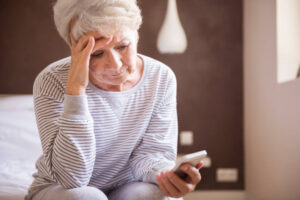 Golpes do INSS: mulher idosa com feições preocupadas olhando para o celular